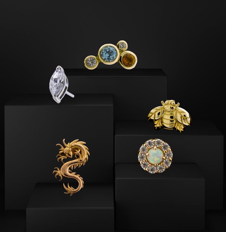 Silicone ear with 18Kt gold jewelry displayed on a gold pedestal with black rocks in the background